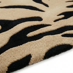 Pu&ograve; includere: Primo piano di un tappeto beige e nero con un motivo a strisce zebrate. Il tappeto ha una superficie morbida e strutturata e una palette di colori neutri, adatta a vari stili di interior design.