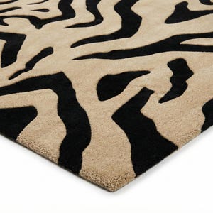 Pu&ograve; includere: Un tappeto beige e nero con un motivo a strisce zebrate. Il tappeto ha una superficie morbida e strutturata e una palette di colori neutri, adatta a vari stili di interior design. Le strisce nere creano un contrasto audace con lo sfondo beige.