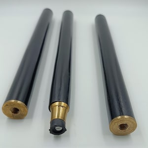 May include: Three black wooden furniture legs with brass-coloured threaded ends. The legs are cylindrical and have a glossy finish. One leg has a rubber foot attached. Suitable for various furniture projects.