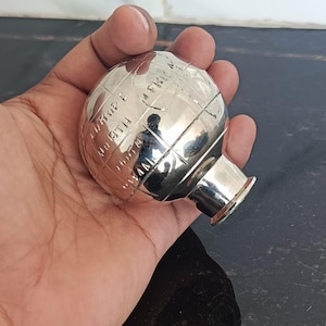 Peut inclure: Un presse-papier globe en métal argenté poli avec des lignes géographiques gravées et du texte incluant Europe, North Africa et d'autres régions. L'objet sphérique possède une base cylindrique plate et une finition de surface réfléchissante.