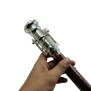 Pu&ograve; includere: Un terminale per asta per tende in metallo argentato e legno. Il terminale presenta un design cilindrico decorativo con un dettaglio a catena. L'asta &egrave; di colore marrone scuro.
