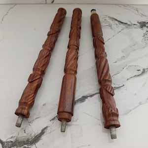 May include: Three intricately carved wooden furniture legs. The legs are a rich, dark brown color with detailed floral and leaf patterns. Each leg has a threaded metal end for attachment. The wood appears to be polished, highlighting the natural grain.