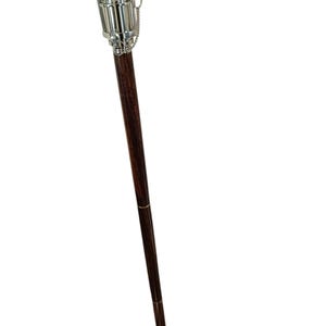 Pu&ograve; includere: Un bastone da passeggio in legno marrone scuro con manico e dettagli in metallo argentato. Il manico ha un design cilindrico con un dettaglio a catena. Un accessorio classico.