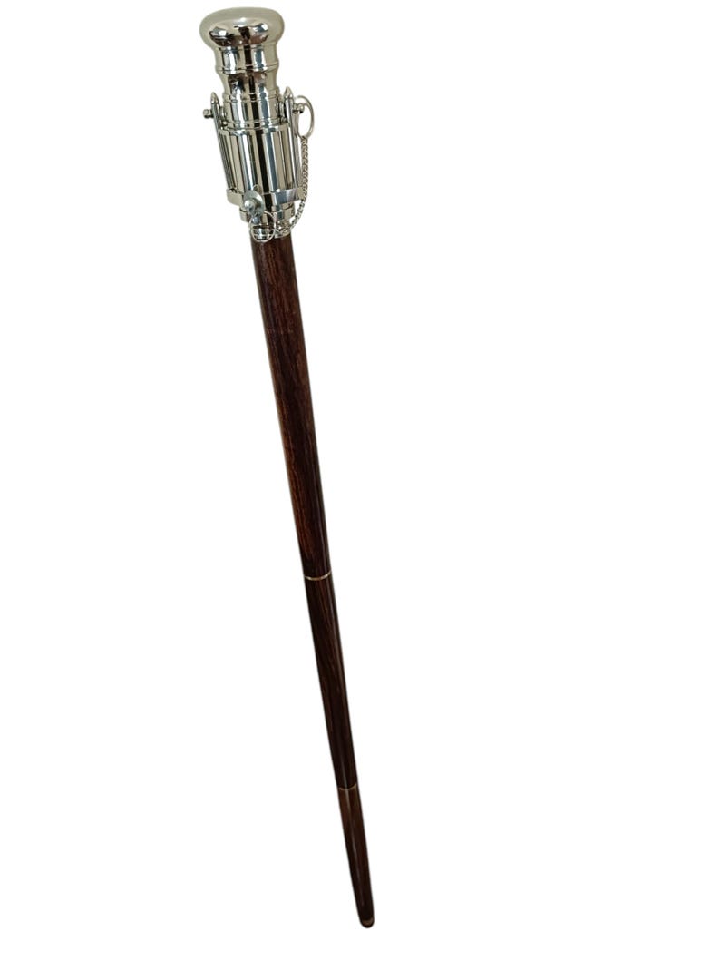 Pu&ograve; includere: Un bastone da passeggio in legno marrone scuro con manico e dettagli in metallo argentato. Il manico ha un design cilindrico con un dettaglio a catena. Un accessorio classico.