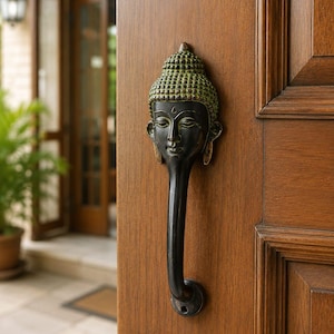 Puede incluir: Un tirador de puerta de metal oscuro con forma de cabeza de Buda y una corona verde texturizada. El tirador presenta una empuñadura larga, lisa y curvada hacia abajo que sale de la barbilla, montada verticalmente en una puerta de madera marrón.