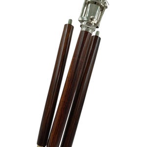 Pu&ograve; includere: Un bastone da passeggio in legno marrone scuro con manico e dettagli in metallo color argento. Il bastone &egrave; parzialmente smontato, con tre sezioni di legno separate visibili. L'impugnatura ha un design decorativo e una piccola catena.