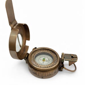 May include: A vintage brass compass with a hinged lid and a clear glass viewing window. The compass face features directional markings and a needle. The compass is open, revealing the internal components.