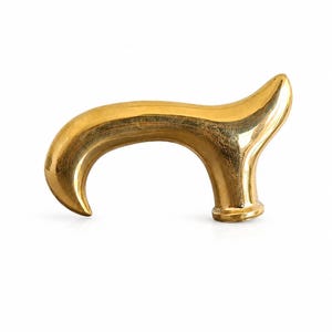 May include: A polished gold-colored cane handle with a smooth, curved, ergonomic shape. The handle features a rounded grip that tapers to a point at one end and a circular base attachment point at the other, showcasing a reflective metallic finish.