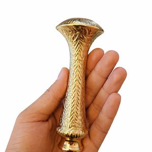 Könnte beinhalten: Eine kleine, goldfarbene Metall-Solitärvase mit ausgestelltem Rand und einem schmalen, zylindrischen Körper. Die Oberfläche ist durchgehend mit einem detaillierten, geprägten Blatt- oder Federmuster versehen und hat einen glatten, abgerundeten Boden.