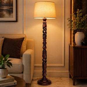 May include: A dark brown wooden floor lamp with a carved, twisted design on the pole. The lamp has a beige fabric lampshade and sits on a round base. The lamp is in a living room setting.