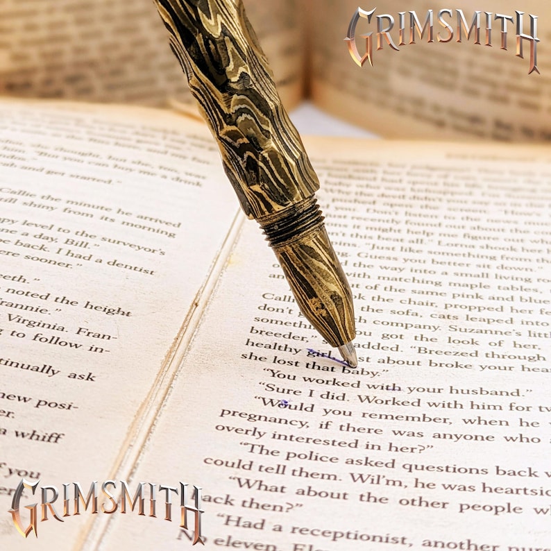 Peut inclure: Gros plan d'un stylo plume Grimsmith avec un motif de grain de bois. Le stylo est dor&eacute; et marron, &eacute;crivant sur un livre avec du texte. Le logo Grimsmith est visible.