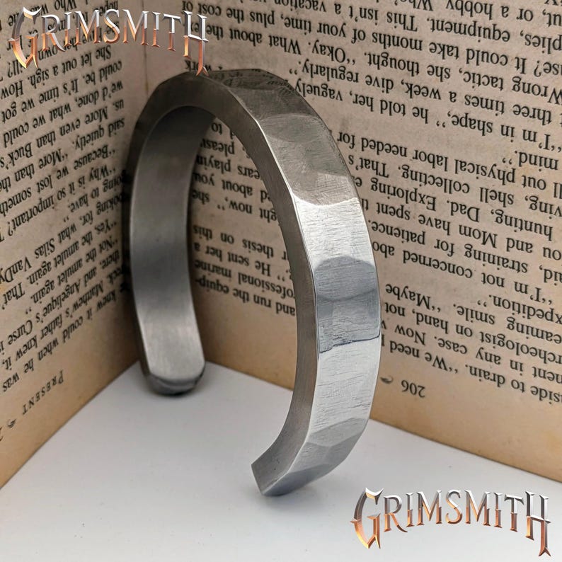 May include: A silver-colored, hammered metal cuff bracelet. The bracelet has a faceted design and a curved, open shape. The word "GRIMSMITH" is visible in the image.