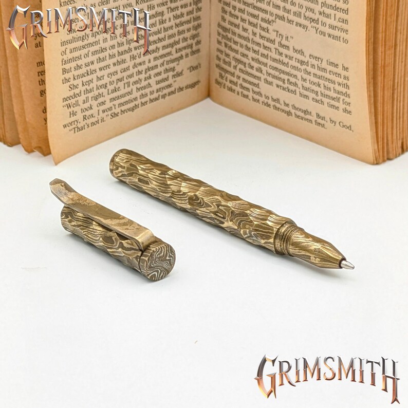 Peut inclure: Un ensemble de stylo et de clip de stylo avec un motif textur&eacute; unique dans des tons or et marron. Le stylo a une pointe m&eacute;tallique &eacute;l&eacute;gante et le clip pr&eacute;sente un design articul&eacute;. Le mot "GRIMSMITH" est affich&eacute; en bas &agrave; droite.