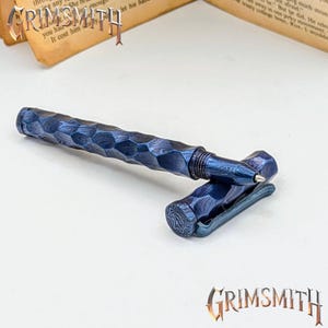 May include: A blue and black pen with a unique geometric pattern. The pen has a matching clip and cap, and the brand name "GRIMSMITH" is visible in the image.