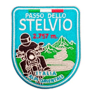 Könnte beinhalten: Gestickter Aufnäher mit türkisfarbenem Hintergrund, mit dem Text "PASSO DELLO STELVIO" und "2.757 m." Ein schwarzes Motorrad und Fahrer sind darunter abgebildet, mit den Worten "ITALIA ALPI ORIENTALI" am unteren Rand. Der Aufnäher hat einen weißen Rand.