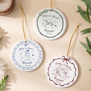 May include: Three round white ceramic ornaments with gold hanging strings. One features green ink with hands and a ring, one blue ink with a couple, and one maroon ink with two champagne glasses. Each includes names, dates, and decorative borders.