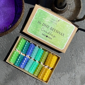 May include: A set of 16 tiny beeswax candles in a brown cardboard box with a green label reading 16 TINY BEESWAX Candles. The candles feature a hexagonal honeycomb texture and come in a gradient of colors including green, blue, teal, and yellow.