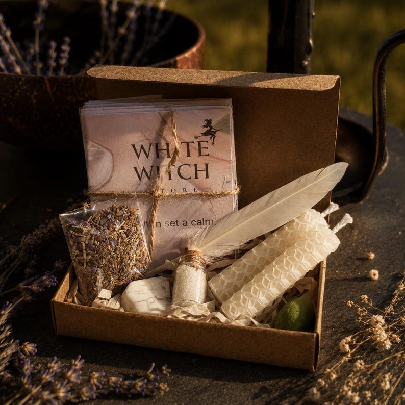 Może przedstawiać: Brązowe kartonowe pudełko prezentowe zawierające stos kart z napisem White Witch, małą plastikową torebkę z suszoną lawendą, białe pi&oacute;ro, małą szklaną fiolkę z białym proszkiem, białą świecę o strukturze plastra miodu oraz biały kamień.