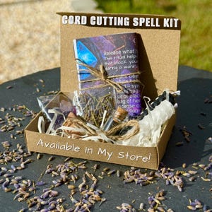 Może przedstawiać: Brązowe kartonowe pudełko z napisem CORD CUTTING SPELL KIT oraz Available In My Store, zawierające wydrukowaną kartę z instrukcjami, małą szklaną fiolkę z korkiem, torebkę suszonej lawendy, fioletowe kryształy i białe wypełnienie z papieru.