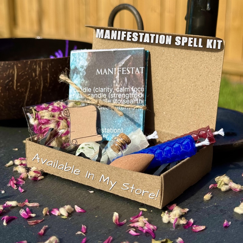 Może przedstawiać: Kartonowe pudełko z napisem MANIFESTATION SPELL KIT zawierające wydrukowaną kartę z instrukcjami, małą torebkę z r&oacute;żowymi płatkami kwiat&oacute;w, szklaną fiolkę z korkiem, kamień w kolorze brązowym oraz dwie teksturowane świece z wosku pszczelego.