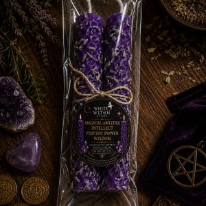 May include: A set of two purple beeswax candles with a honeycomb texture and embedded dried lavender, wrapped in clear plastic. A circular label features the text White Witch Store, Magical Abilities, Intellect, Psychic Power, Wisdom, and Set of 2.