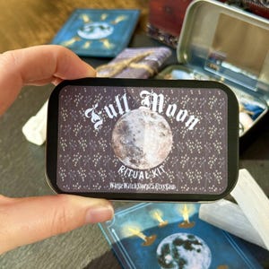May include: A rectangular tin with a black background and the words "Full Moon Ritual Kit" in white script. The tin features a detailed image of the moon. Other items are visible in the background.