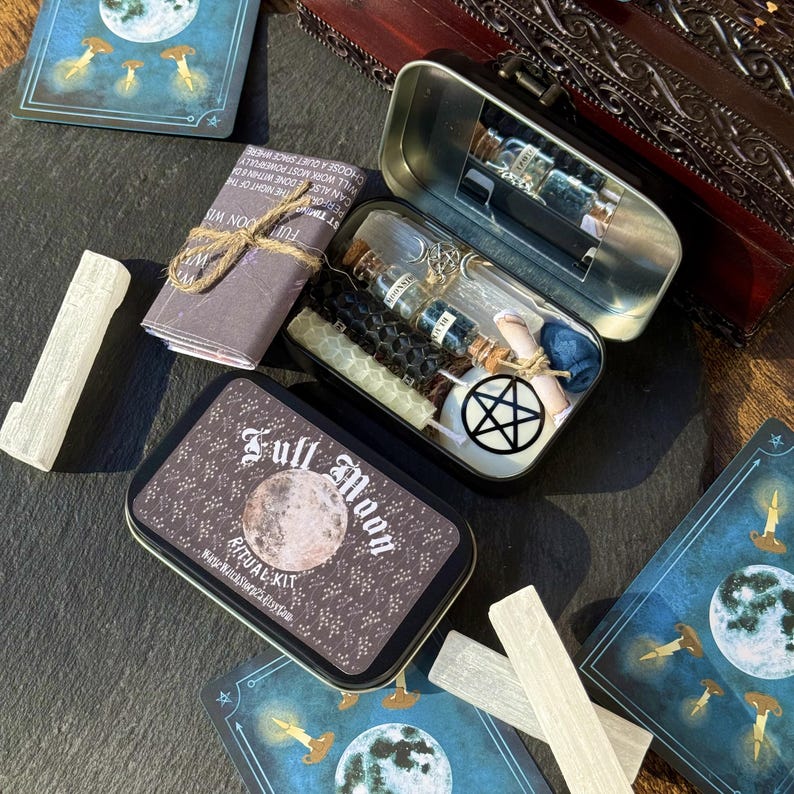 May include: A Full Moon Ritual Kit in a decorative tin, featuring a moon graphic and text. The kit includes candles, small bottles, a pentagram, and other ritual items. Additional items include cards with moon and candle illustrations, and a white crystal.