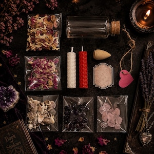 May include: A collection of ritual supplies including dried flower petals in clear bags, a glass vial with a cork, two honeycomb-textured candles in white and red, an incense cone, a blank label, a pink heart tag, seashells, and crystals.