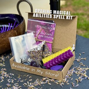 Może przedstawiać: Brązowe kartonowe pudełko zawierające zestaw zaklęć Opening Magical Abilities, w tym fioletowo-ż&oacute;łtą świecę z wosku pszczelego o strukturze plastra miodu, woreczek suszonej lawendy, srebrny wisiorek z pentagramem i fioletowy kryształ.