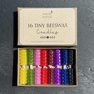 May include: A cardboard box containing 16 tiny beeswax candles in various colors including yellow, green, pink, red, dark red, purple, blue, and black. The box lid features the text White Witch Store, 16 Tiny Beeswax Candles, and Made Especially For Short Rituals.