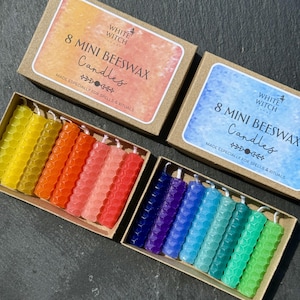May include: Two rectangular cardboard boxes containing eight mini beeswax candles each. One box has an orange label reading 8 MINI BEESWAX Candles, the other a blue label reading 8 MINI BEESWAX Candles. The candles feature a hexagonal honeycomb texture.