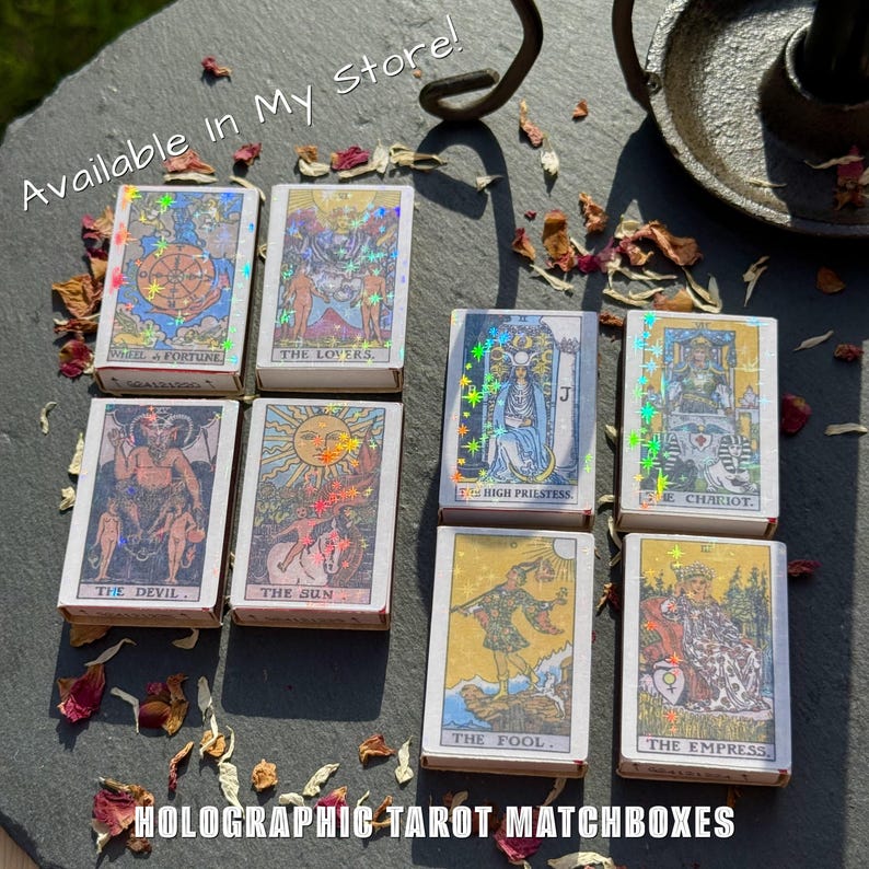 May include: A collection of holographic tarot matchboxes, each featuring a different card design. The matchboxes are white with colorful holographic accents and text. The text "Available in My Store!" and "HOLOGRAPHIC TAROT MATCHBOXES" are visible.