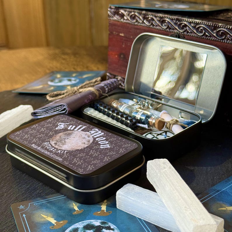 May include: A Full Moon Ritual Kit in a black tin with a full moon design. The kit includes a variety of items, such as candles, crystals, and a small tin with a mirror. Other items include a small scroll, a black beaded bracelet, and tarot cards.