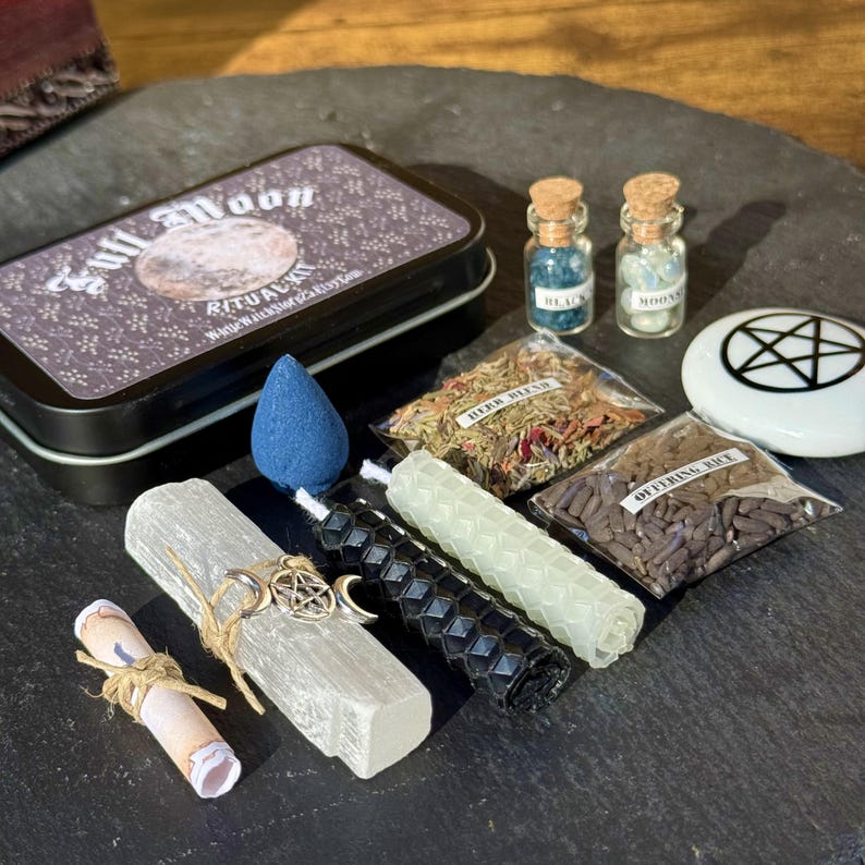 May include: A collection of ritual items including a black tin with "Full Moon Ritual Kit" text, small glass bottles, bags of herbs and rice, candles, a blue incense cone, and a white stone with a pentagram symbol.