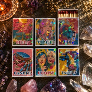 Może przedstawiać: Sześć prostokątnych pudełek z zapałkami z holograficznymi ilustracjami znaków zodiaku. Pudełka przedstawiają wzory i napisy Libra, Virgo, Leo, Cancer, Gemini oraz Taurus w żywych kolorach. Jedno pudełko jest otwarte, ukazując zapałki z czerwonymi łebkami.