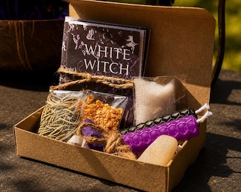 May include: A brown cardboard box containing a White Witch booklet, dried herbs, orange granules, a white sponge, and two hexagonal textured candles in black and purple, all tied together with brown twine for a compact kit presentation.