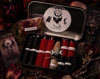 May include: A metal tin containing several small hexagonal candles in red and black, a small glass bottle, and a silver-toned pentagram charm. The lid features a circular sticker with an owl, a winged figure, and the text LILITH. Nearby are printed cards with illustrations of a winged figure and the text LILITH, along with a small bag of dried herbs.