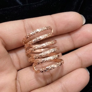 May include: A rose gold spiral ring with an intricate floral pattern. The ring wraps around the finger multiple times, creating a unique and eye-catching design. The ring is made of a shiny metal.