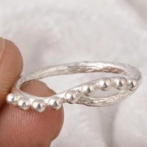 Puede incluir: Una taza de cerámica blanca con asa negra y el texto "But First, Coffee" en negrita negra. La taza se encuentra sobre un fondo borroso, resaltando su diseño limpio.