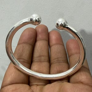 May include: A silver cuff bracelet with a rounded design. The bracelet has a smooth, polished finish and spherical accents at each end. The open design allows for easy wear.