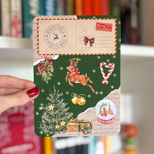 May include: A rectangular Christmas card with a green background and festive illustrations. The card features a reindeer, Christmas tree, snow globe, and the text "North Pole Express Mail". A red bow and the words "Merry Christmas" are also visible.