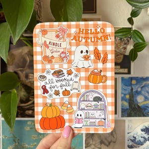 May include: A rectangular sticker sheet with an orange and white gingham pattern. The sheet features various autumn-themed illustrations, including pumpkins, ghosts, and the text "Hello Autumn!" and "all booked for fall."