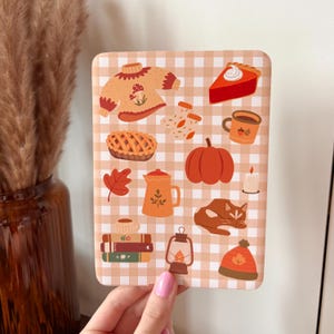 Può includere: Un motivo a quadri beige e bianco con illustrazioni a tema autunnale. Le illustrazioni includono un maglione, torta, zucca, tazza di caffè, foglia, gatto, libri, lanterna e un cappello.