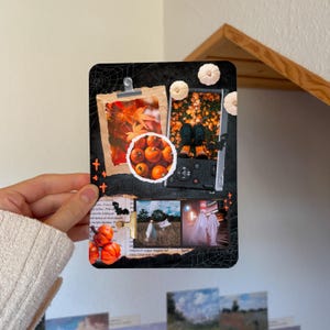 May include: A rectangular collage print featuring a black background with spiderweb patterns, orange pumpkins, and autumn leaves. It includes multiple framed photographs of fall scenes, ghosts, and foliage, accented with small orange cross symbols.