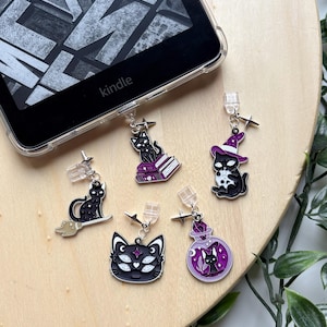 May include: A selection of black cat charms with silver details, including a cat on a broom, a cat on books, and a cat in a witch hat. The charms are attached to clear plastic clips, suitable for use with an e-reader.