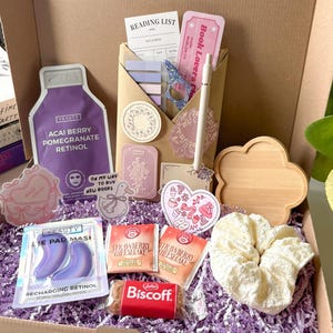 Può includere: Una confezione regalo piena di articoli per la cura di sé e per la lettura. Include una maschera per il viso viola, patch per gli occhi, snack al cheesecake alle fragole, un biscotto Biscoff, un elastico per capelli, adesivi e una lista di lettura.