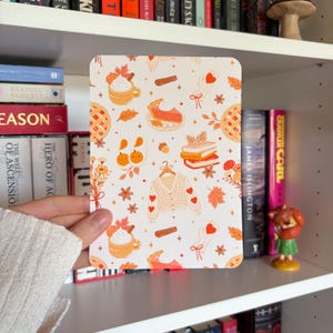 May include: A rectangular art print featuring a repeating pattern of autumn-themed illustrations including orange pumpkins, mugs of whipped cream, slices of pumpkin pie, stacks of books, a knit cardigan, fallen leaves, and cinnamon sticks.