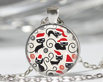 May include: A round silver pendant necklace featuring a repeating pattern of black cats wearing red and white Santa hats on a cream background, interspersed with small red and grey yarn balls, suspended from a silver-toned metal link chain.