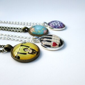 May include: Four round pendant necklaces with silver and bronze chains. The pendants feature diverse imagery including a yellow illustration of a person lifting weights, a piano keyboard with a red heart, a blue world map, and a purple Om symbol.