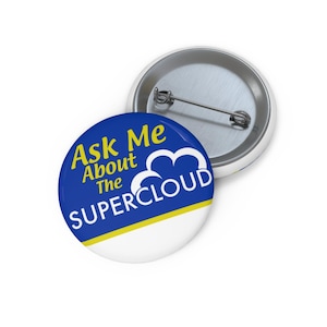 May include: Two round buttons with a pin back. One button is in focus, featuring the text "Ask Me About The SUPERCLOUD" in yellow and white on a blue background. The other button is partially visible, showing the pin back and a white border.